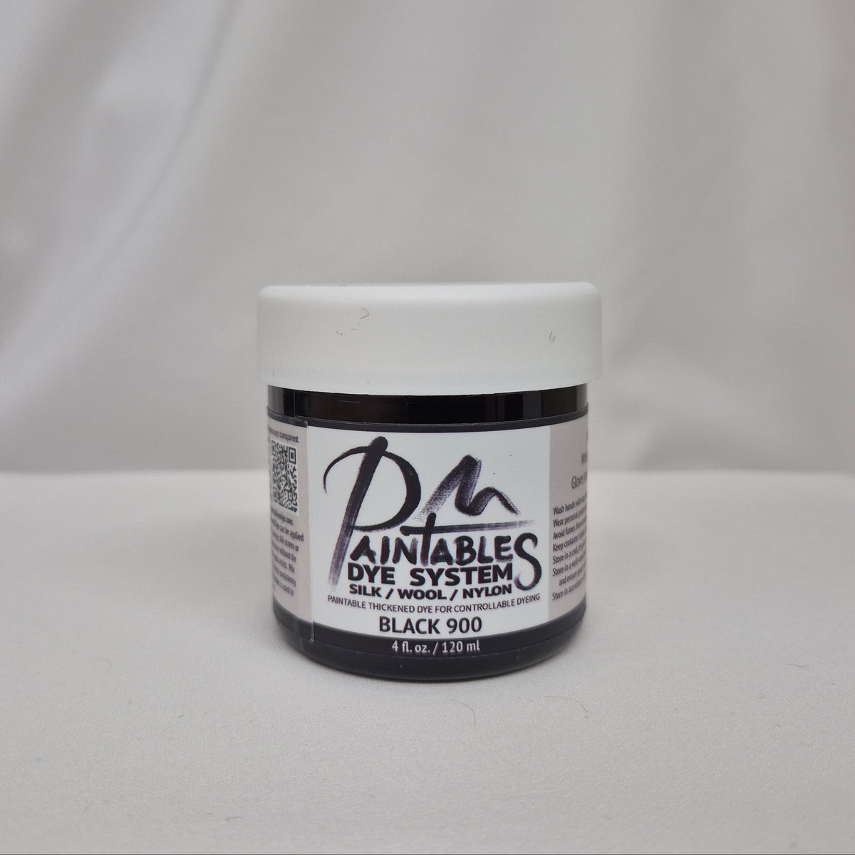 A jar of Paintables Dye System Black 900 dye, featuring a white lid and a black-and-white label, set against a draped white fabric background.