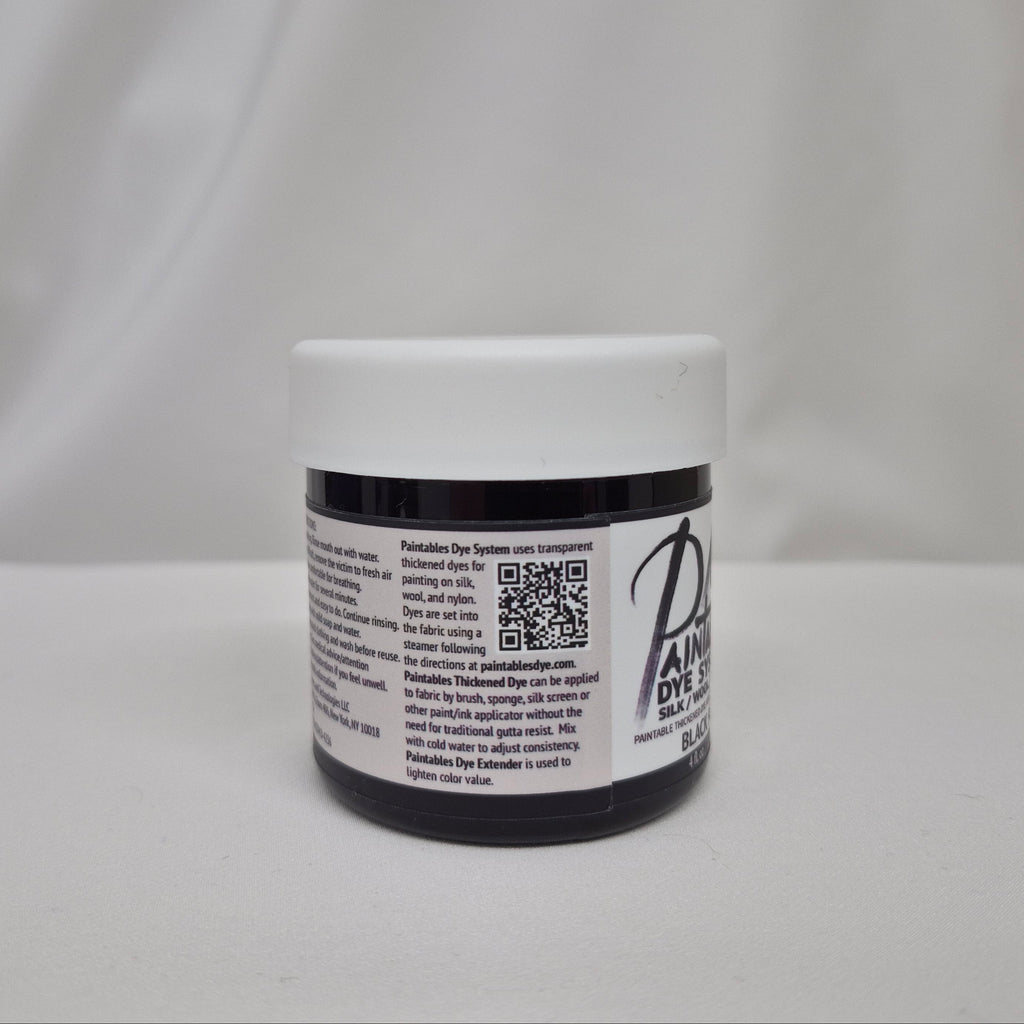 A small plastic jar of black liquid with a white screw cap, showing the side label with information on Paintables Dye System, set against a draped white fabric background.
