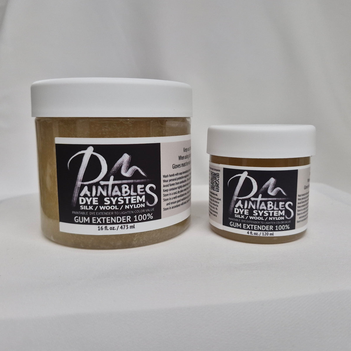 A 16oz white plastic jar of Paintable Dye System Gum Extender 100% and a 4oz white plastic jar of Paintable Dye System Gum Extender 100% on a white fabric background.
