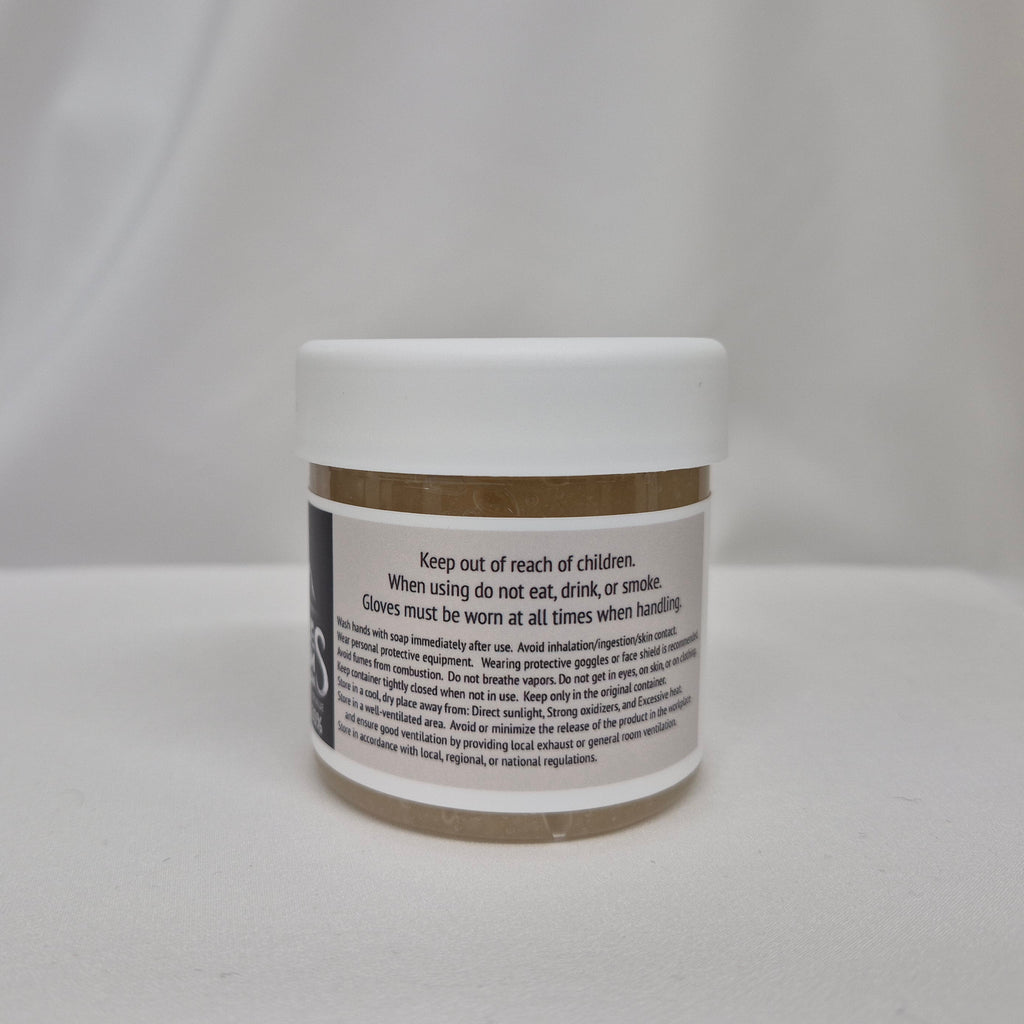 A small white plastic jar with a gum extender thickener inside, a white lid, and black label featuring black text containing safety instructions, set against a draped white fabric background.