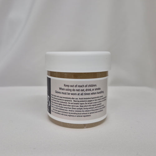 A small white plastic jar with a gum extender thickener inside, a white lid, and black label featuring black text containing safety instructions, set against a draped white fabric background.