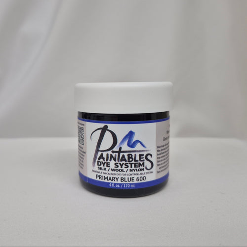 A jar of Paintables Dye System Primary Blue 600 dye, featuring a white lid and a white label with blue and black text, set against a draped white fabric background.