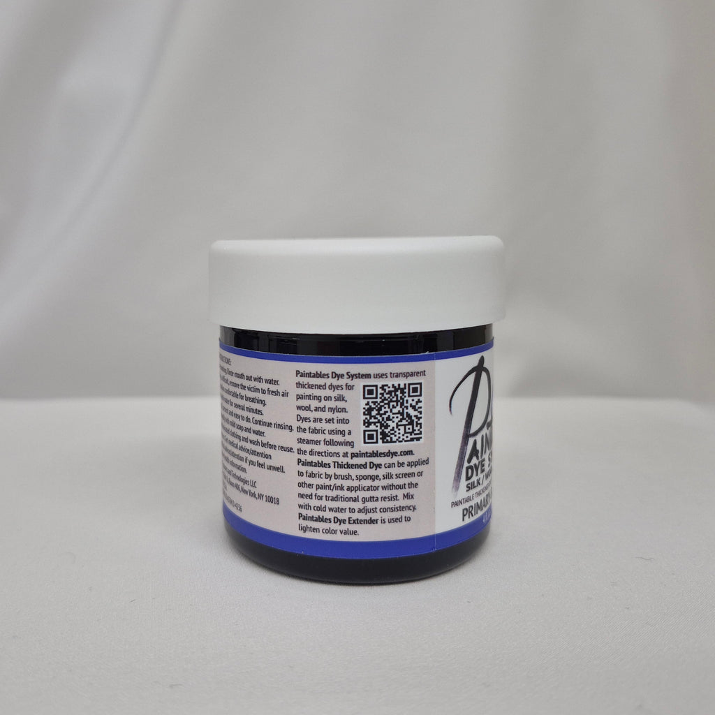A small plastic jar of deep blue liquid with a white screw cap, showing the side label with info on Paintables Dye System, set against a draped white fabric background.
