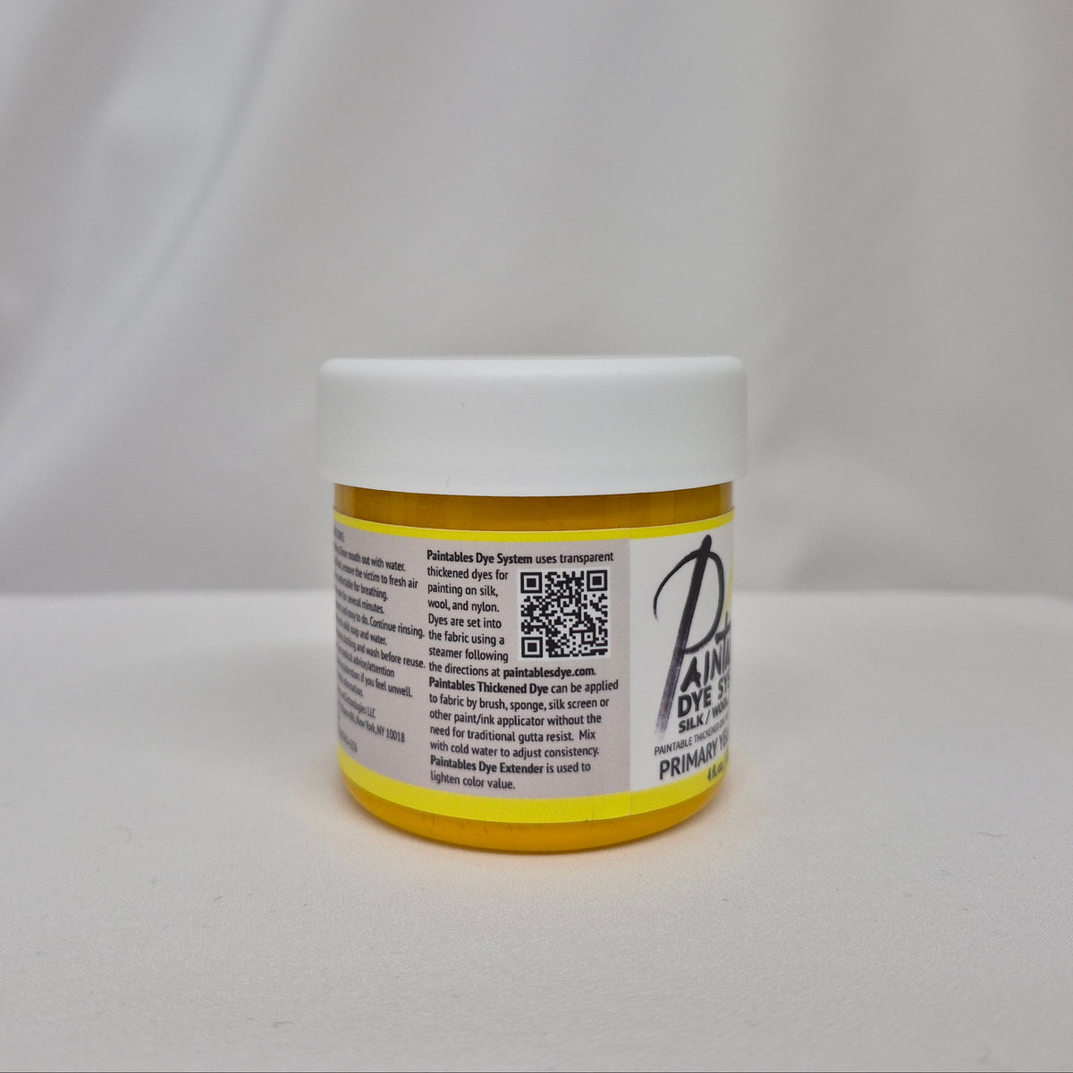A small white plastic jar with a yellow lid and a white label featuring black text and a QR code, set against a draped white fabric background.
